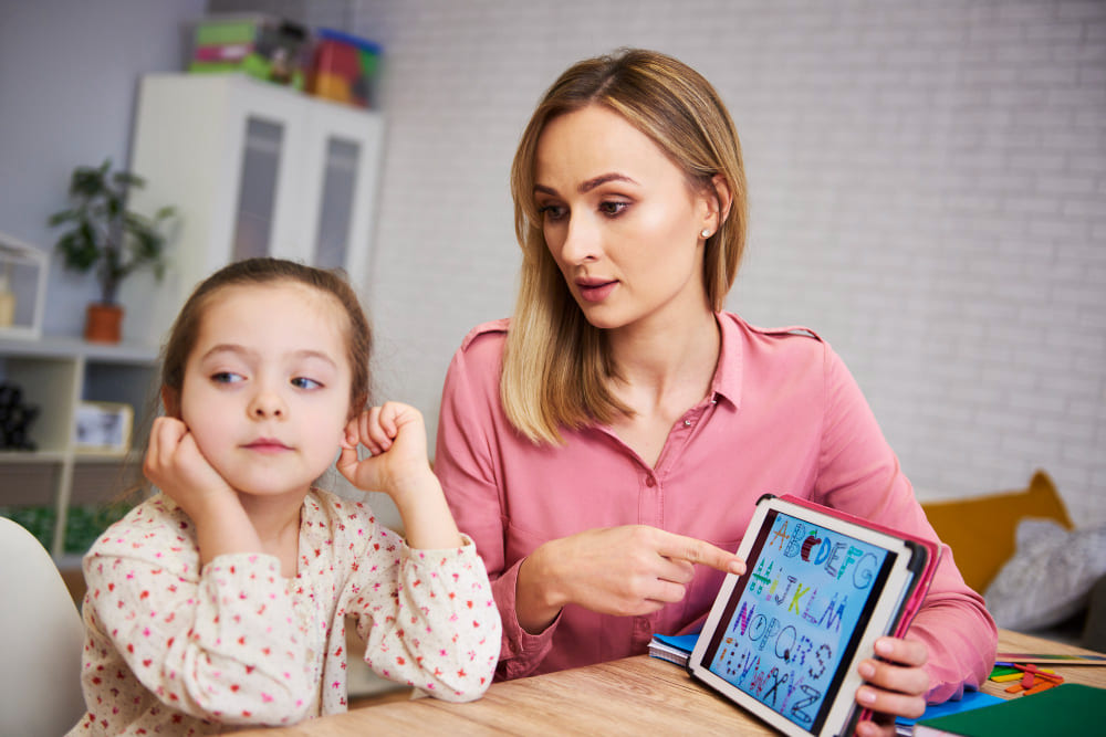 Mulher mostra uma atividade no tablet para meninas que não presta atenção
