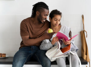 Pai com filha no colo e livro na mão se preparando para a escola