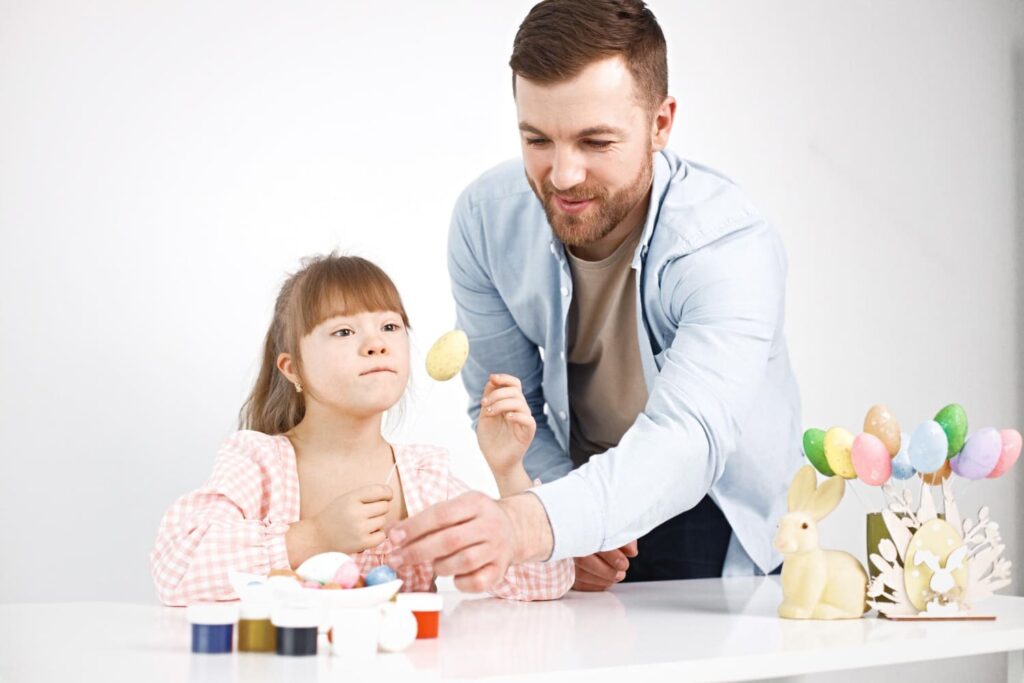 menina com síndrome de down e seu pai brincando com ovos coloridos de pascoa 